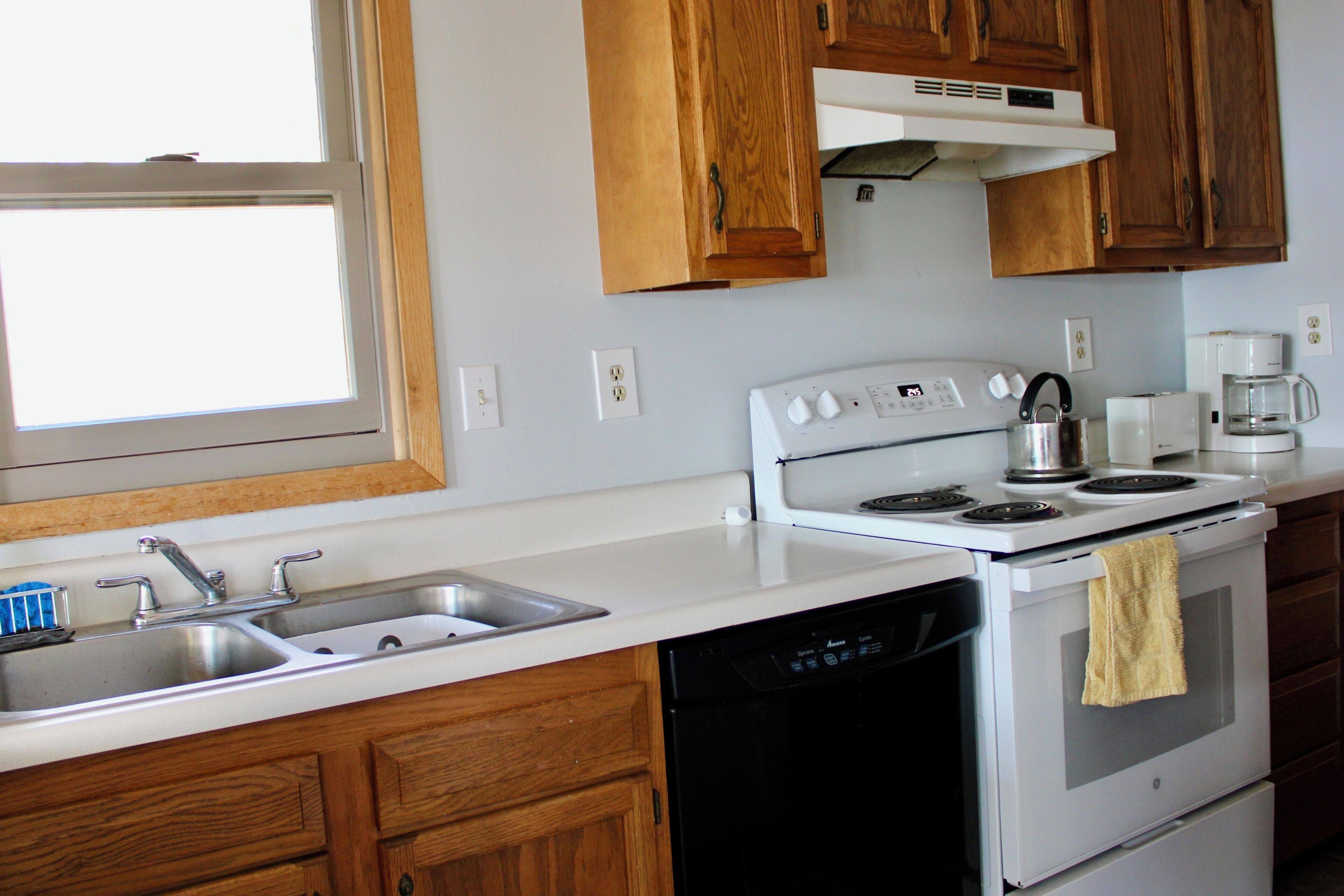 A kitchen with wooden cabinets, a white stove, a dishwasher, and a sink.