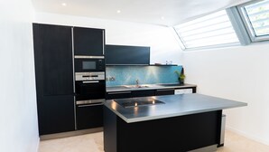 Une cuisine moderne avec des meubles de couleur noire, un îlot central en acier inoxydable et un dosseret de carrelage bleu.