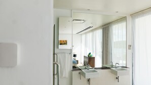Une salle de bain moderne avec deux lavabos, un grand miroir et une vue sur une chambre à coucher comprenant un lit et une table de chevet.