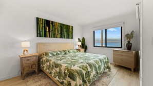 A bedroom with a bed, a nightstand, a bedside lamp, a window with a view, and a decorative plant.