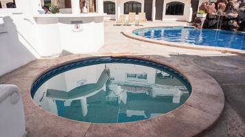 Área de piscina com duas piscinas distintas, uma com borda circular e outra com formato retangular tradicional. Há espreguiçadeiras e uma pequena cascata.