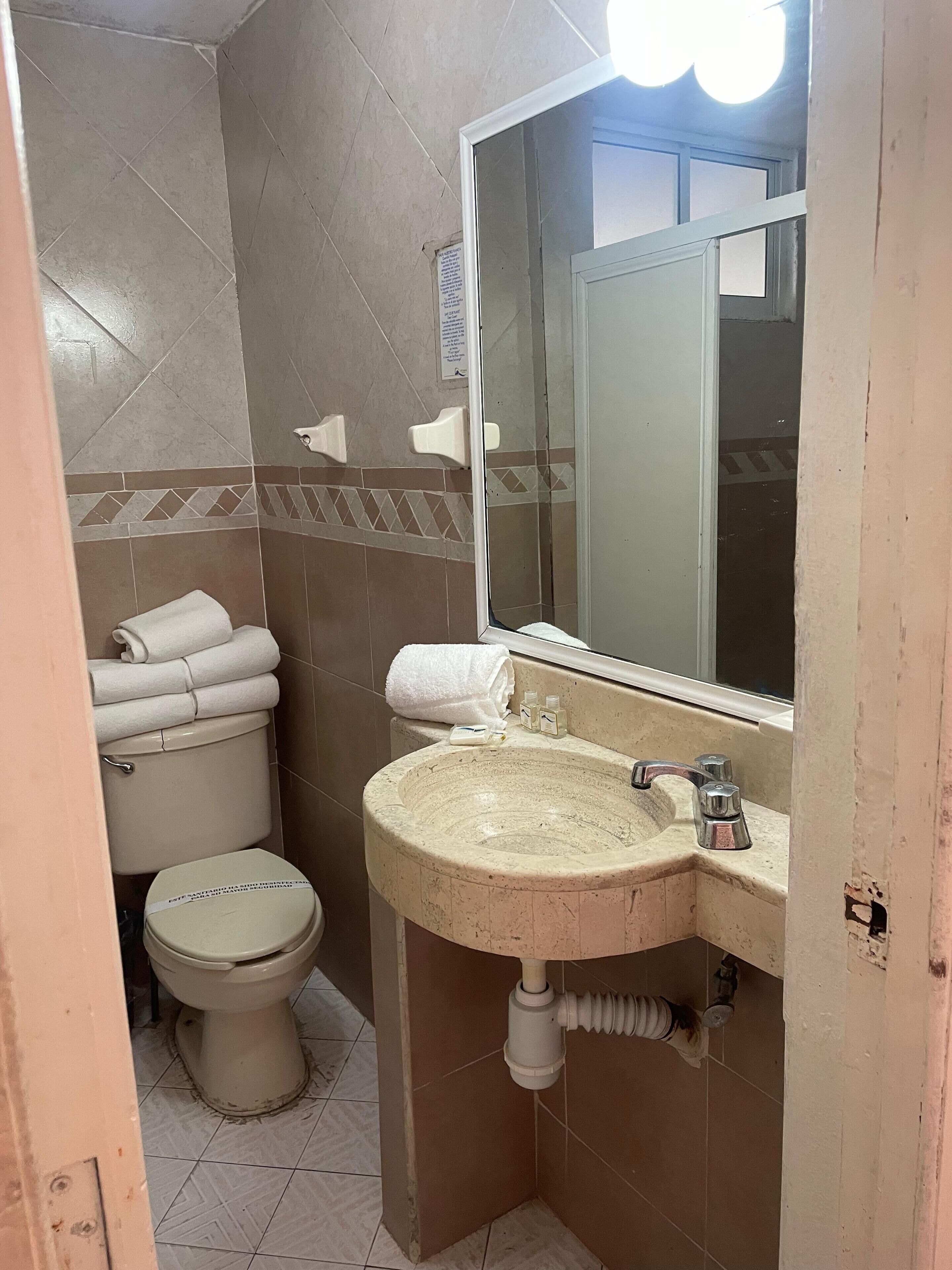 A small bathroom with a toilet, sink, and mirror. There are towels stacked on the toilet and a hand dryer on the wall.