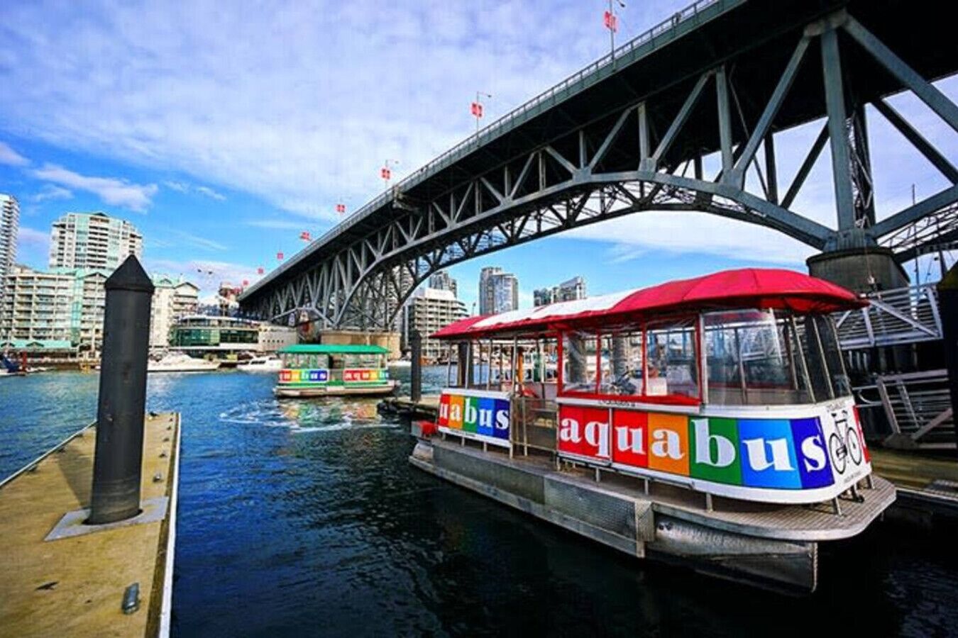Un bote con la marca 'aqua bus', un puente y edificios de la ciudad al fondo.