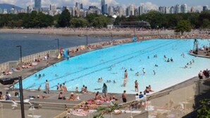 A large public swimming pool with people swimming and sunbathing, surrounded by a city skyline and a beach. - Kitsilano Getaway - Near Beach - 10 min to Downtown (Vancouver)