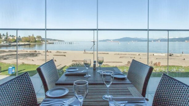 A dining table with chairs and wine glasses, overlooking a beach and water. - Kitsilano Getaway - Near Beach - 10 min to Downtown (Vancouver)