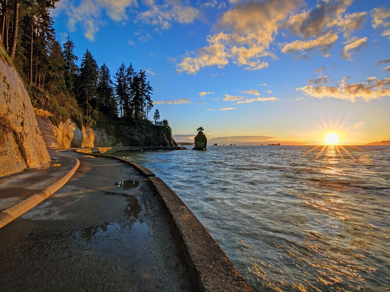 A coastal road with a rocky cliff and a view of the ocean at sunset.