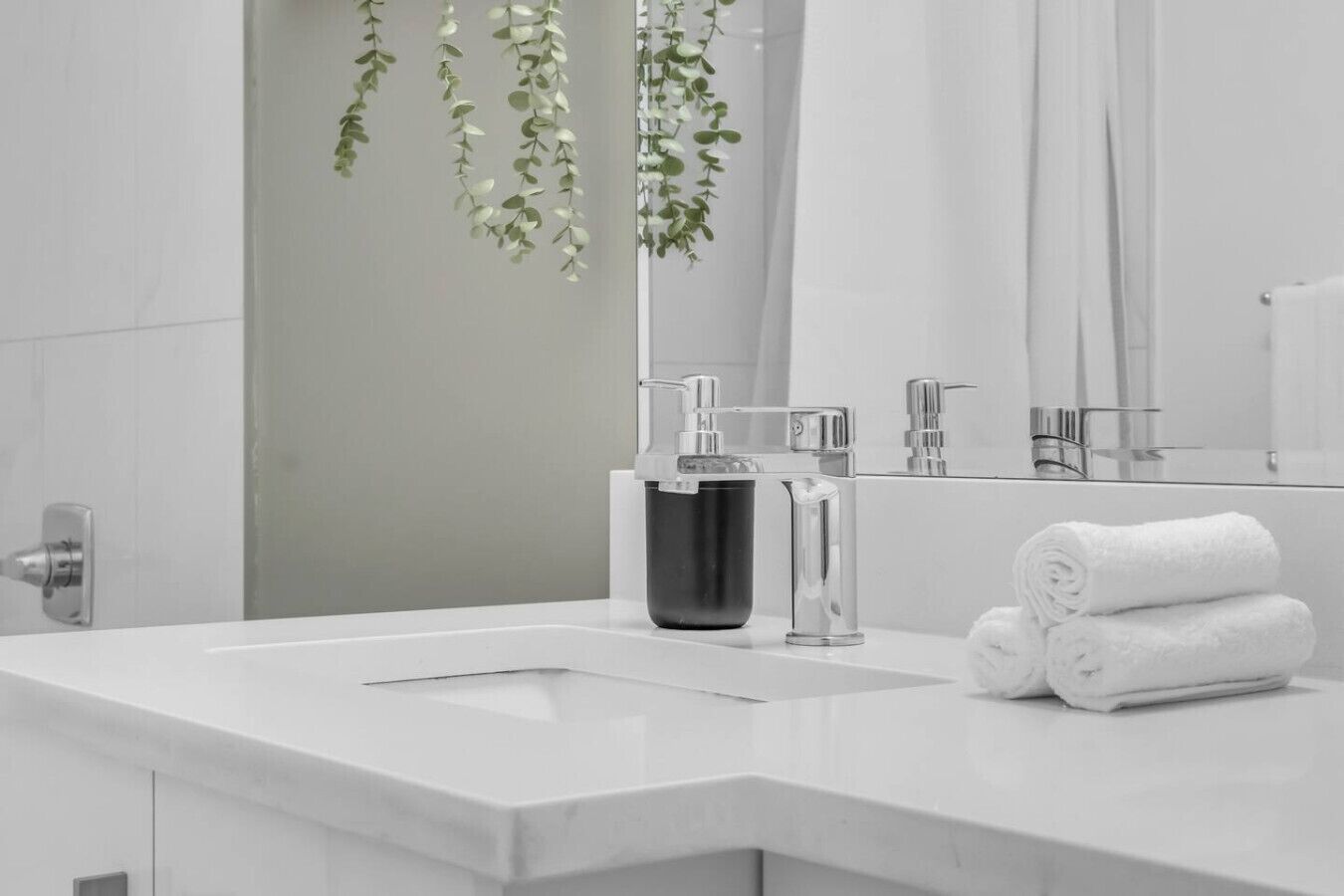 A modern bathroom with a white sink, chrome faucet, and a mirror reflecting a shower.