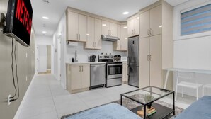 A modern kitchen with a built-in oven, refrigerator, and microwave. There is a dining area with a glass table and blue sofa. - Kitsilano Getaway - Near Beach - 10 min to Downtown (Vancouver)