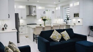 Una cocina moderna con armarios blancos, una isla central, iluminación colgante y un sofá azul oscuro con cojines estampados.