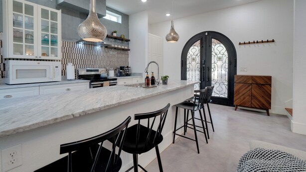 Una cocina moderna con encimera de mármol, taburetes negros y luminarias colgantes.