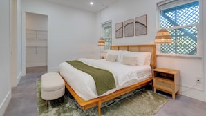 Un dormitorio con cama de madera, manta verde, mesita de noche blanca y ventana con diseño de celosía.
