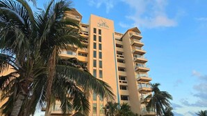 A hotel with a pool, palm trees, and a clear sky. - Beach & Nightlife Paradise; Top floor and ocean view (Cancún)