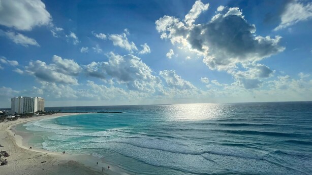 A beach with a hotel in the background, clear skies, and calm ocean waves. - Beach & Nightlife Paradise; Top floor and ocean view (Cancún)