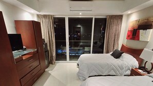 A hotel room with two beds, a ceiling fan, a TV, a wardrobe, and a view of the city at night. - Beach & Nightlife Paradise; Top floor and ocean view (Cancún)