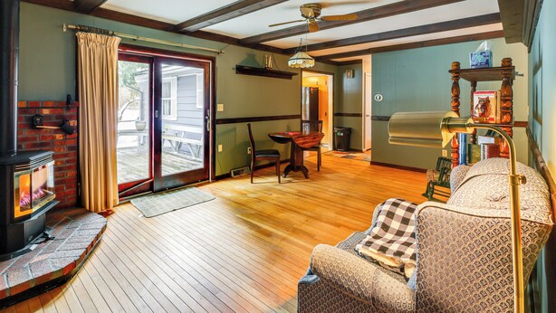 A cozy living room with a fireplace, wooden flooring, a sofa, and a ceiling fan. - 9 Mi to Lake George Village: Home in Queensbury (Queensbury)