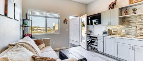 A modern living room with a sofa, a dining area with a kitchen, and a large window.