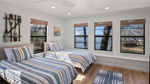 A bedroom with two beds, a ceiling fan, and large windows with blinds.