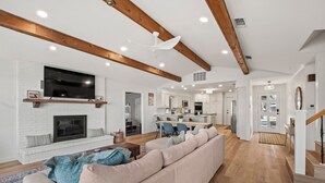 A spacious living room with a fireplace, a large TV mounted on the wall, and a modern kitchen in the background.