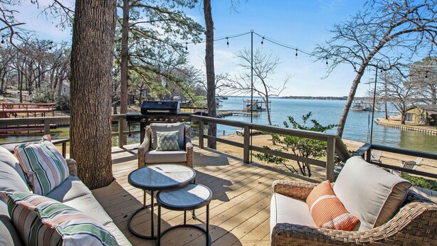 A deck with outdoor furniture, a grill, and a view of a lake.