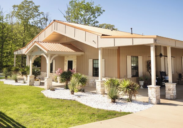 A two-story house with a covered porch, stone pillars, and a landscaped front yard with various plants. - Charming Farmhouse, Hot Tub, Pool, Outdoor Kitchen, Farm animals & Stocked Pond. (Diana)