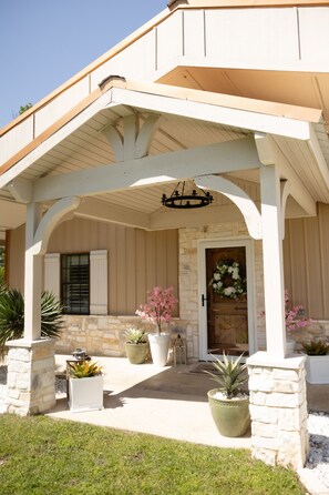 A covered porch with a stone wall, a wooden door with a floral wreath, and potted plants. - Charming Farmhouse, Hot Tub, Pool, Outdoor Kitchen, Farm animals & Stocked Pond. (Diana)