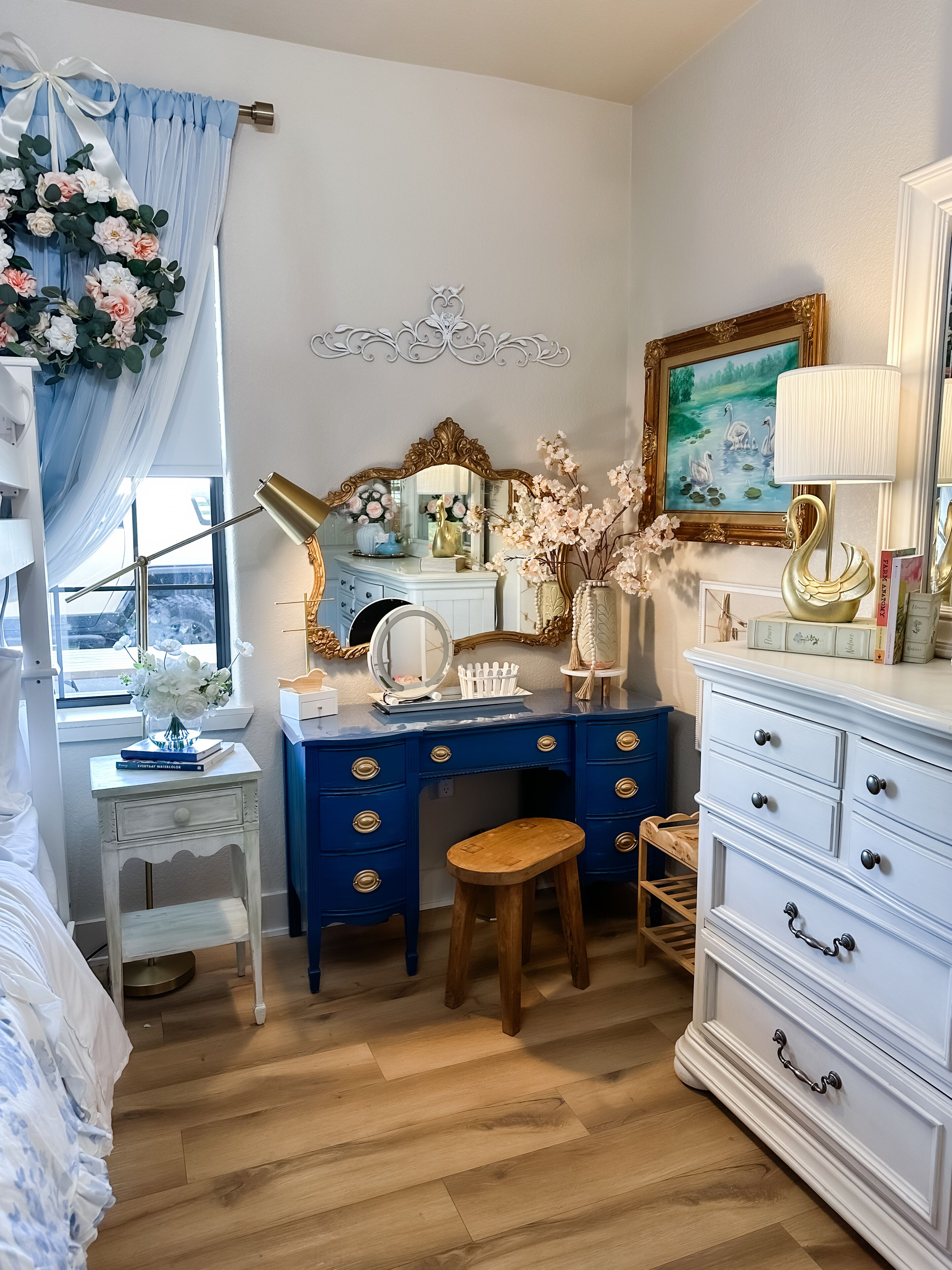 A bedroom with a vanity, a dresser, a bed, and a window with curtains.