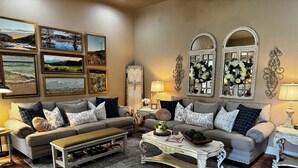 A living room with a grey sofa set, a coffee table, and a fireplace. There are framed pictures on the wall and a decorative mirror. - Charming Farmhouse, Hot Tub, Pool, Outdoor Kitchen, Farm animals & Stocked Pond. (Diana)