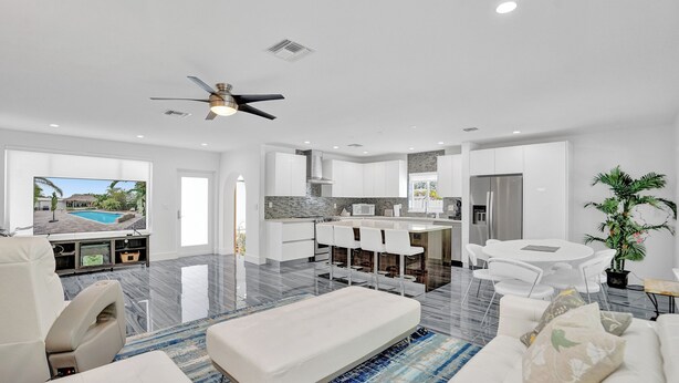 A modern living room with a large TV, a sofa, a coffee table, and a dining area with a table and chairs. - Daddy House (Fort Lauderdale)