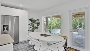 A modern kitchen with white cabinetry, a stainless steel refrigerator, and a dining area with a white table and chairs. - Daddy House (Fort Lauderdale)