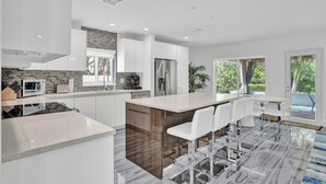 A modern kitchen with a central island, white cabinetry, and a view of the outdoors. - Daddy House (Fort Lauderdale)