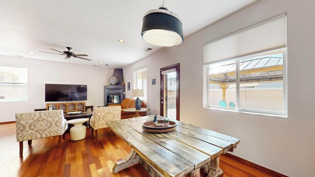 A spacious living room with a wooden dining table, patterned chairs, a ceiling fan, and a large window with a view of the outside.