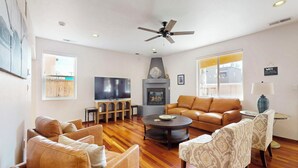 A spacious living room with a large flat-screen TV, leather sofas, a fireplace, and a ceiling fan.