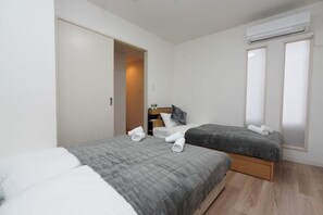 Een slaapkamer met twee bedden, een kledingkast, een nachtkastje en een airconditioning.