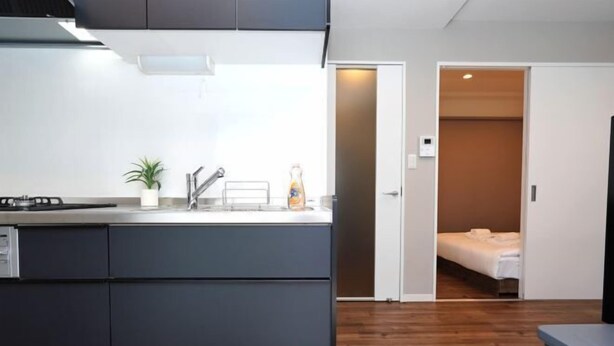 Une cuisine compacte équipée d’une cuisinière, d’un évier et de placards, qui donne sur une chambre avec un lit et une porte.