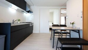 Une cuisine moderne avec des meubles de couleur sombre, un coin repas avec une table et des chaises, et une porte visible donnant sur une autre pièce.