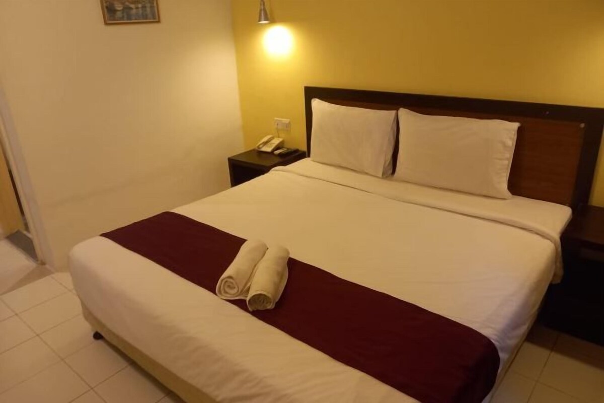 A neatly made bed with white and maroon bedding, a folded towel, and a bedside phone on a nightstand.