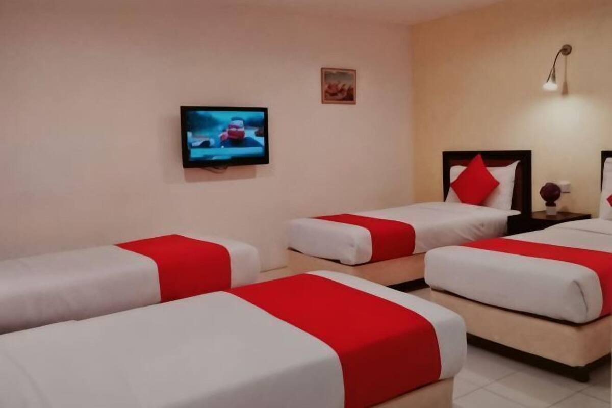 Ein Hotelzimmer mit drei Betten, einem Fernseher, einer Lampe und einem kleinen Tisch.