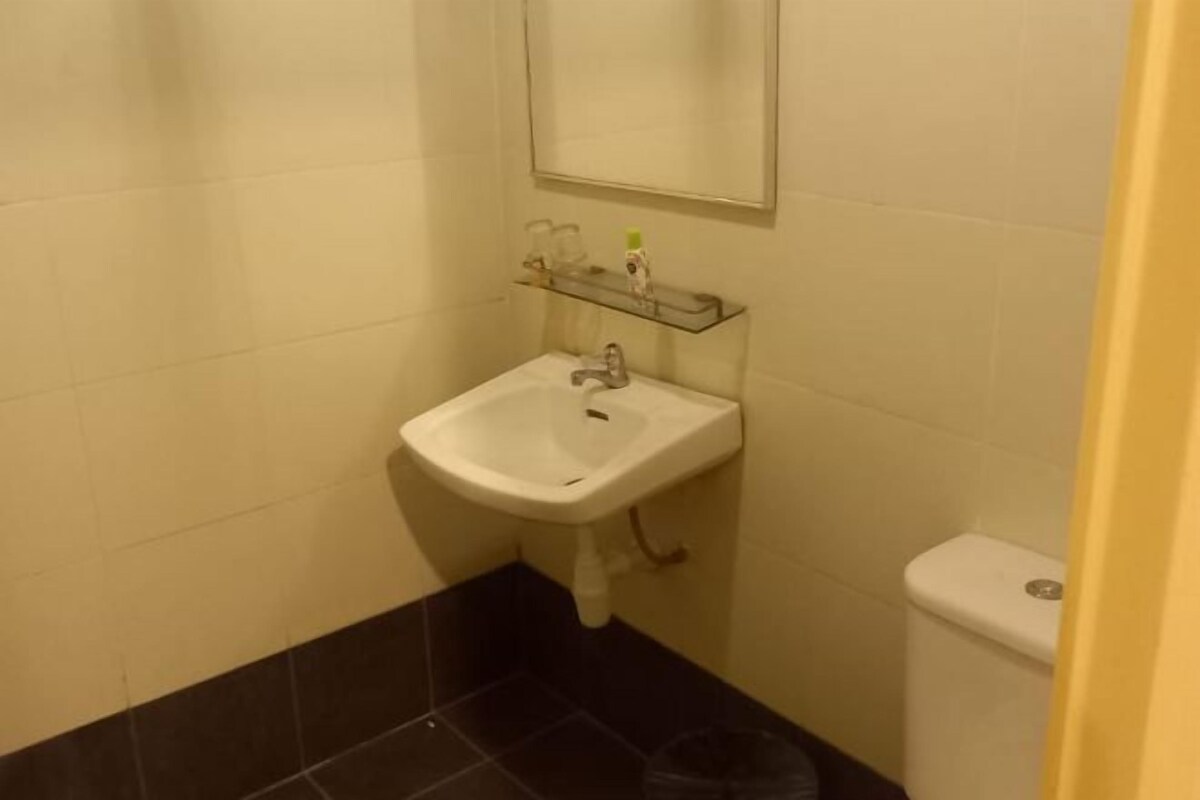 Un baño con un lavamanos blanco, un espejo encima y un inodoro a la derecha.