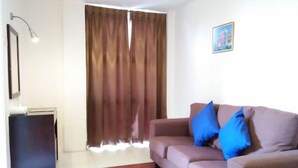 A living room with a sofa, a lamp, a picture on the wall, and a window with curtains. - Syajie Koptown Hotel (Segamat)