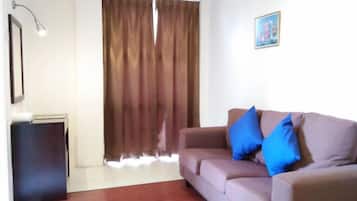 A living room with a sofa, a lamp, a picture on the wall, and a window with curtains.