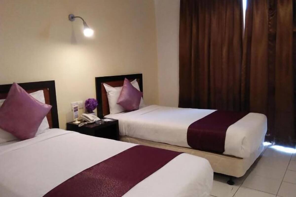 Ein Hotelzimmer mit zwei Betten, jeweils mit Kopfteil, einem Nachttisch mit Telefon und einer Wandlampe.