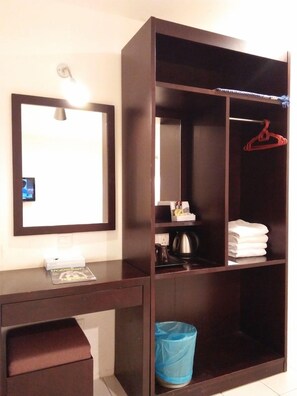 A room with a large wardrobe, a desk with a lamp, a mirror, and a trash bin.