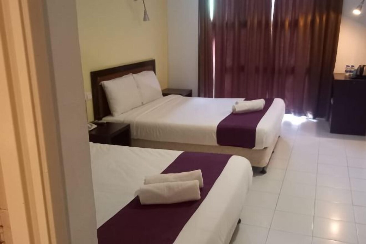 A hotel room with two beds, a desk, and a window with curtains.