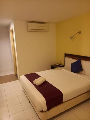 A hotel room with a bed, a bedside table, a wall-mounted air conditioning unit, and a door. - Syajie Koptown Hotel (Segamat)