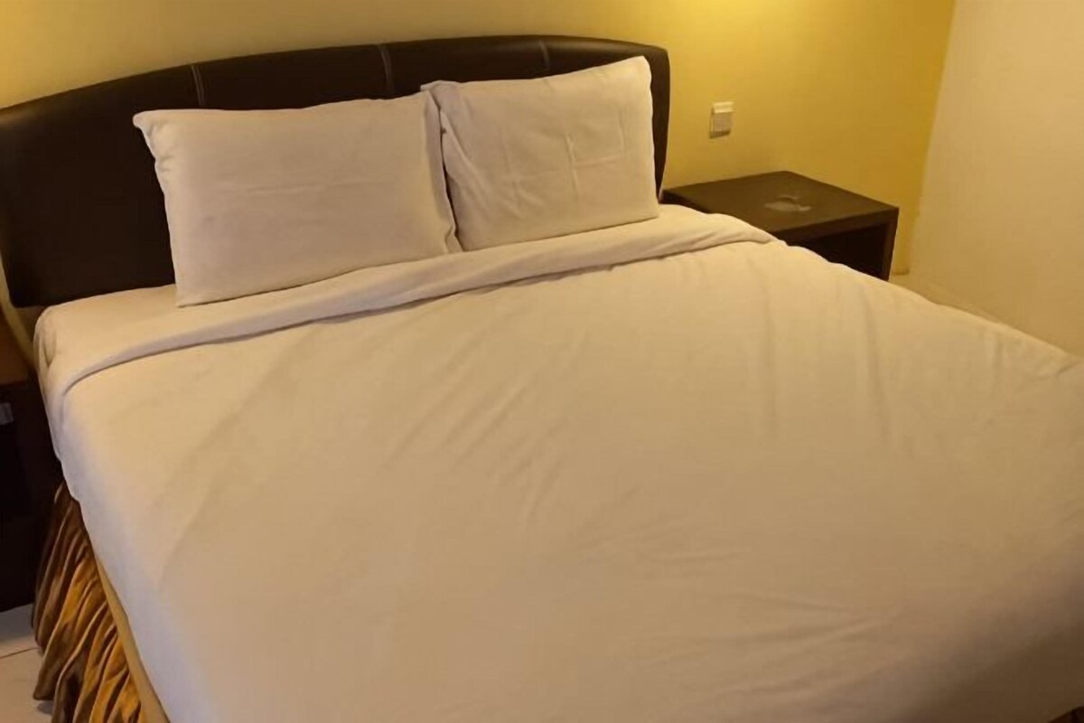A bed with white bedding, a dark headboard, and a nightstand with a lamp.