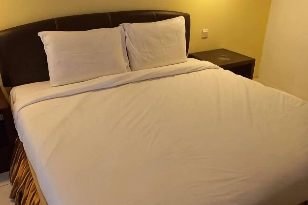 Ein Bett mit weißer Bettwäsche, einem dunklen Kopfteil und einem Nachttisch mit Lampe.