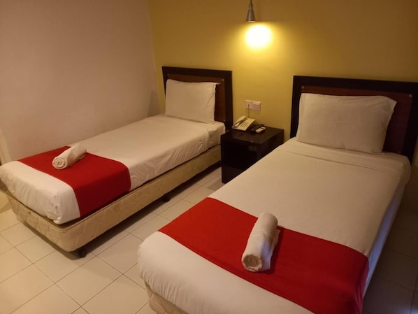 Two single beds with red and white bedding, a bedside table with a phone, and a wall-mounted light fixture.