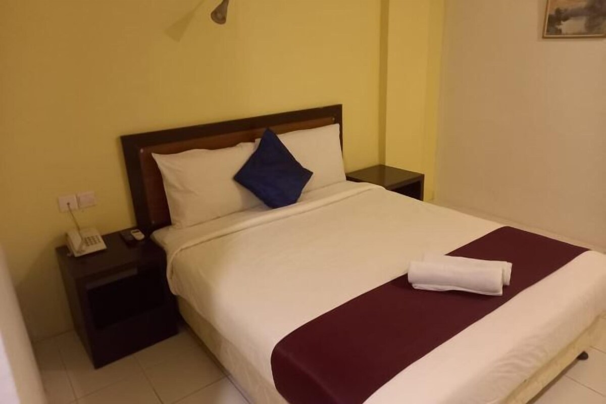 A neatly made bed with a white and maroon bedspread, a blue pillow, and a folded white towel on the bed.