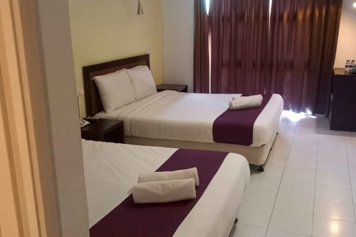 A hotel room with two beds, a nightstand, a desk, and a window with curtains.