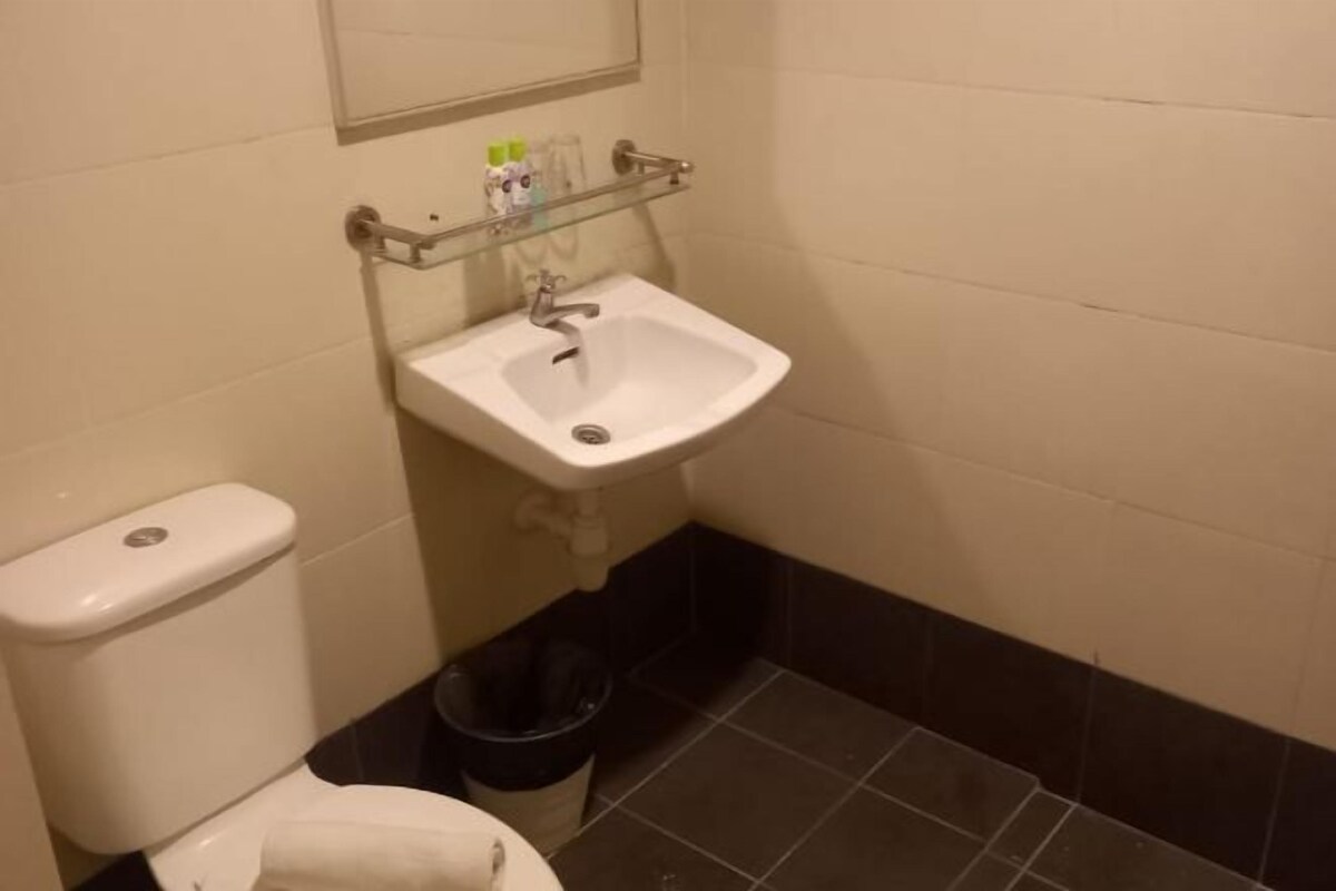 A bathroom with a white sink, a toilet, a trash bin, and a mirror above the sink.